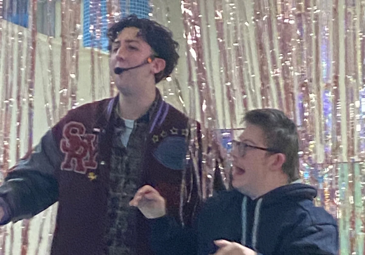 Un ragazzo canta e balla sul palco insieme a un intrattenitore, durante una festa di Carnevale.