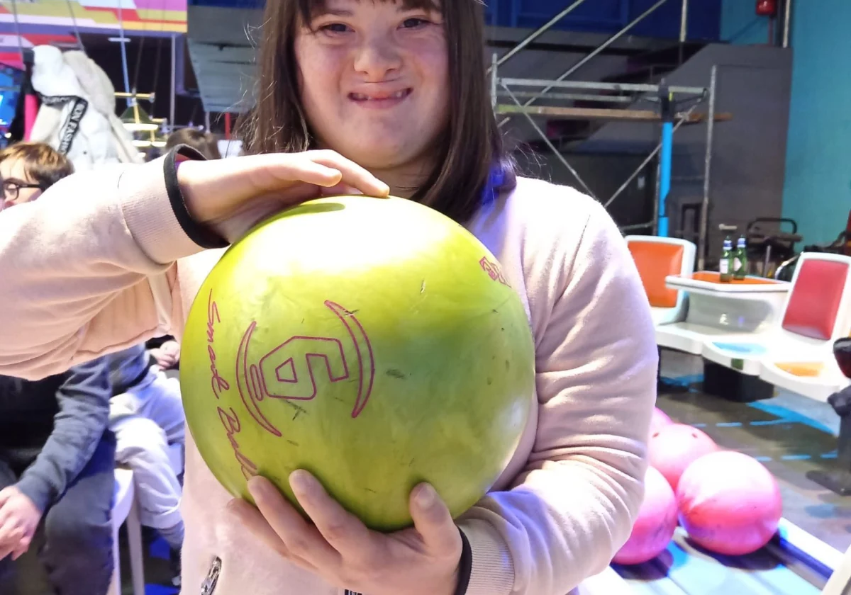 Una ragazza sorridente tiene in mano una palla da bowling, in una sala giochi.