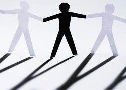 Sagome di cartone a forma di persone stilizzate che si tengono per mano, una al centro di colore diverso dalle altre.