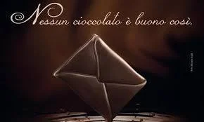 Un cioccolatino a forma di busta su sfondo scuro, con la scritta "Nessun cioccolato è buono così".