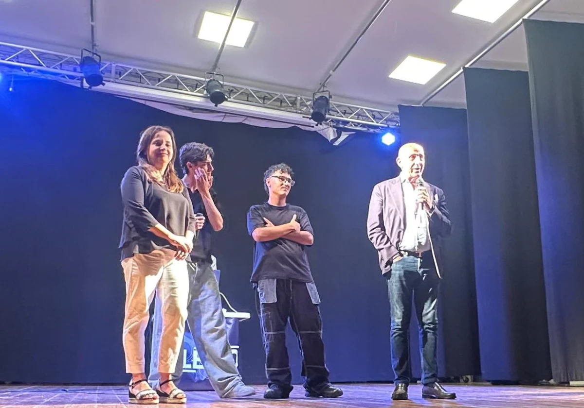 Quattro persone su un palco, una delle quali parla al microfono, durante la serata di musica e solidarietà.