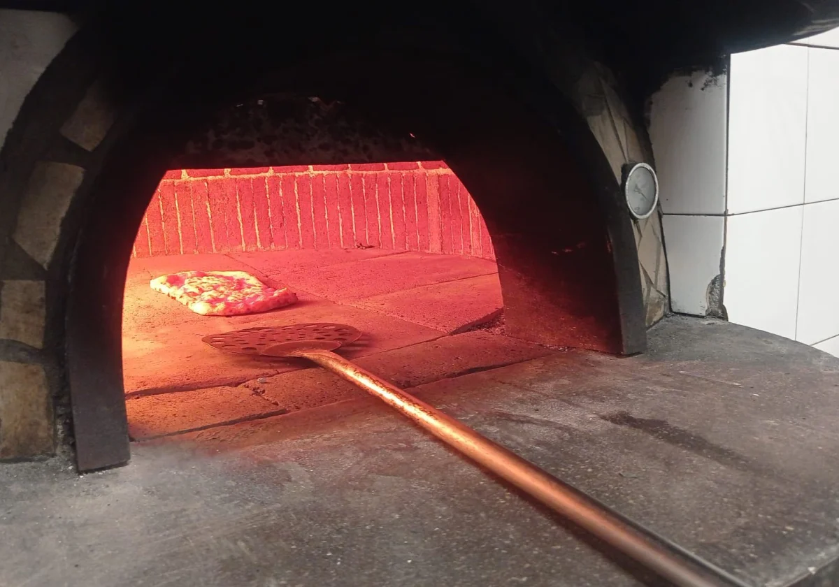 Una pizza che cuoce in un forno a legna, con la pala del pizzaiolo in primo piano.