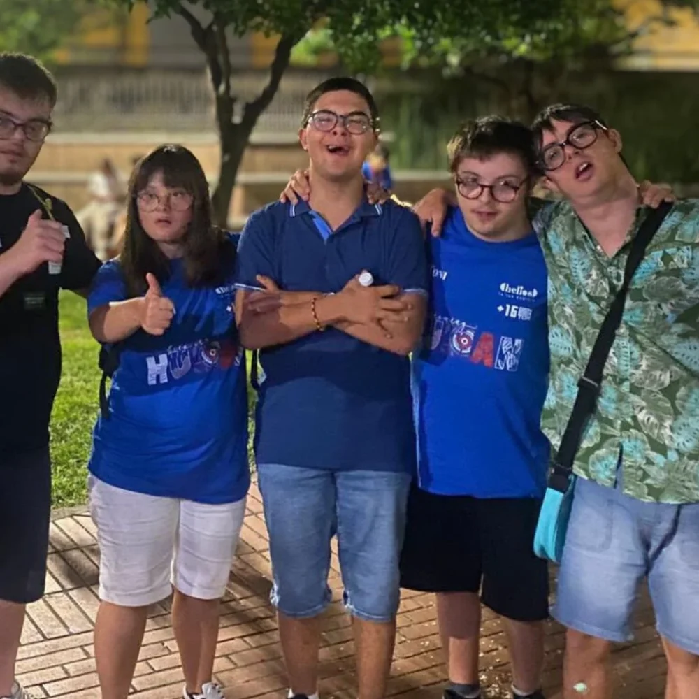 Un gruppo di ragazzi e ragazze si abbraccia sorridendo durante una serata all'aperto.